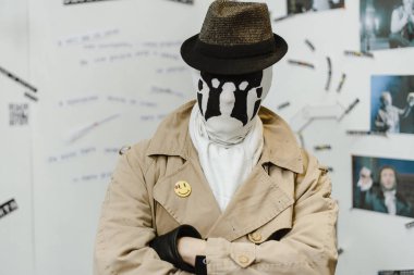A man in a mask with rorschach stains and a coat is standing in a room with evidence. Comic detective clipart