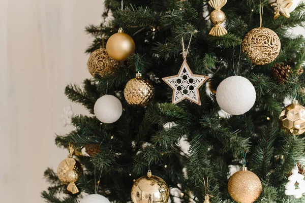 Goud en wit Kerstbal op een kerstboom in een licht interieur tegen de achtergrond van brandende bloemenslingers van verlichting. Decoreren kerstboom op heldere achtergrond — Stockfoto