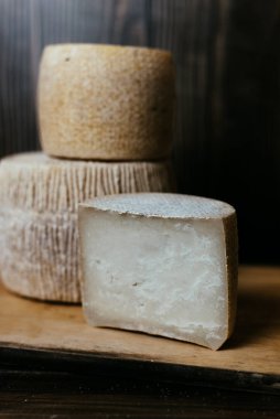 Koyu ahşap arka planda farklı ev yapımı peynirler. Kravot, manchego ve Paramezan 'ın peynir başları. Kâğıt üzerinde keçi ve inek peyniri. El işi. Kapat.