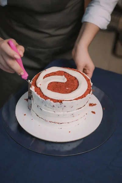 O confeiteiro nivela o creme no bolo. O cozinheiro cria um bolo, recolhe-o e cobre-o com creme e depois nivela-o com uma espátula e um raspador. — Fotografia de Stock