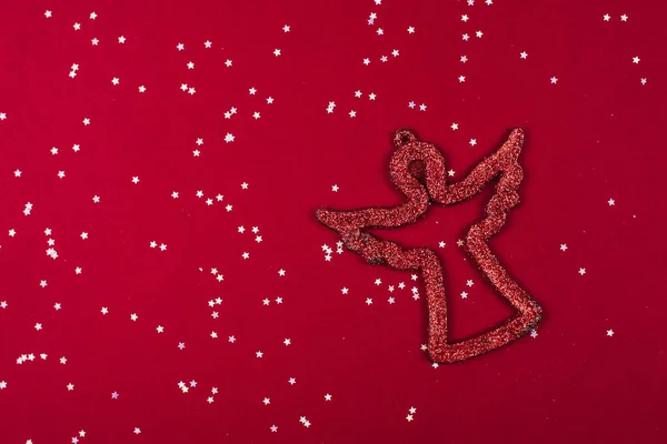 Símbolo rojo brillante de ángel y cristianismo sobre fondo rojo con estrellas plateadas de confeti. Símbolo de la Navidad Católica y Año Nuevo. Colocación plana, copyspace — Foto de Stock