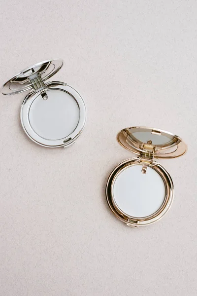 Pequeños espejos de bolsillo cosméticos redondos en oro y plata sobre un fondo beige. Espejos de bolsillo con lugar para texto, publicidad. Plantilla para diseñadores — Foto de Stock