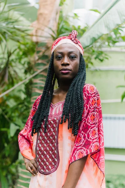 Een mooie jonge Afro-Amerikaanse vrouw staat onder palmbomen in de jungle en glimlacht breed in een nationaal Afrikaans kostuum. Gevoelig outdoor portret van het aantrekkelijke Afrikaanse meisje met oogschaduwen — Stockfoto