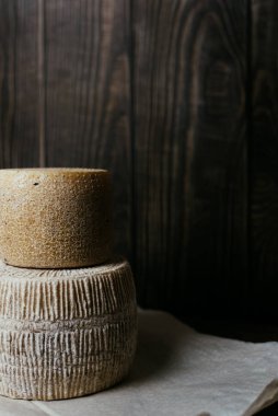 Koyu ahşap arka planda farklı ev yapımı peynirler. Kravot, manchego ve Paramezan 'ın peynir başları. Kâğıt üzerinde keçi ve inek peyniri. El işi. Kapat.