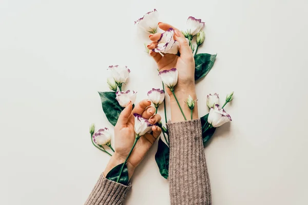 Delicate hands and spring flowers of eustoma are on the white table. the concept of skin care. Natural cosmetics for hand skin care, a means to reduce wrinkles on the hands, moisturizing. Natural flow