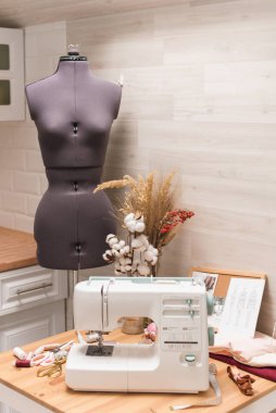 The workplace of a seamstress. Sewing machine on the table, thread, scissors and mannequin