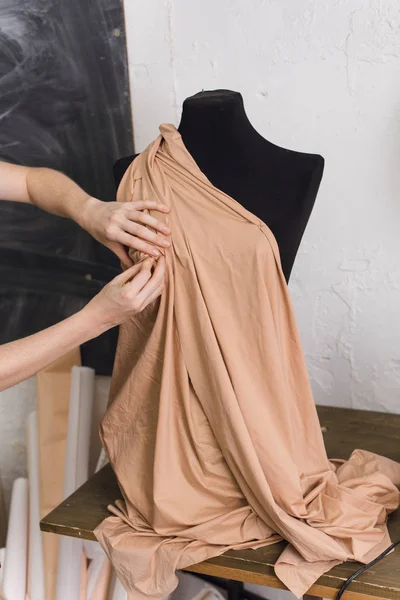 Швея примеряет ткань на черном манекене в швейной мастерской. Дизайнер проектирует платье из бежевой ткани и создает одежду. портниха прикрепляет ткань к манекену с иглами. cre — стоковое фото