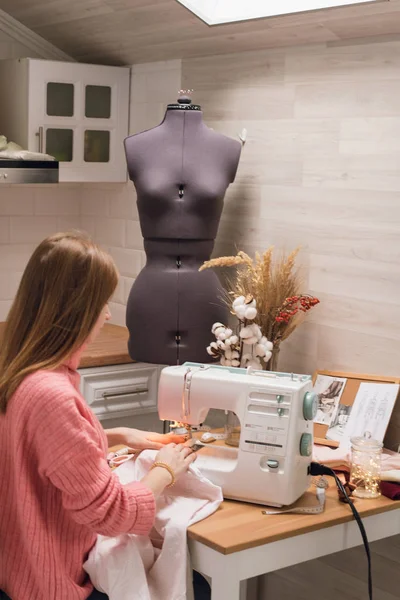 La costurera trabaja en una máquina de coser. La chica cose y sostiene un paño rosa — Foto de Stock
