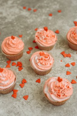 Pink cupcakes on a gray background for Valentine's day. Gift sweets with cream and sprinkle with hearts