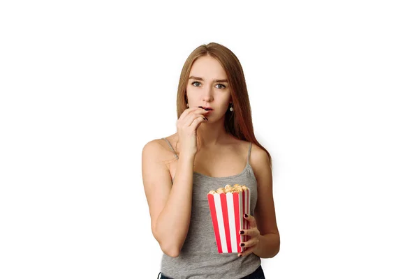 Linda chica sosteniendo palomitas de maíz y mirando a la cámara aislada en un estudio blanco. Mujer emocionada teniendo palomitas de maíz mientras ve la película en el fondo blanco —  Fotos de Stock