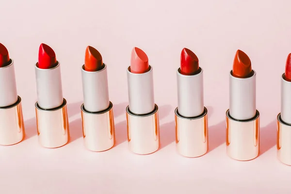 Multi-colored lipsticks stand in a row on a pink background. The concept of different, collections and beauty. Red, pink and burgundy lipsticks — Stock Photo, Image