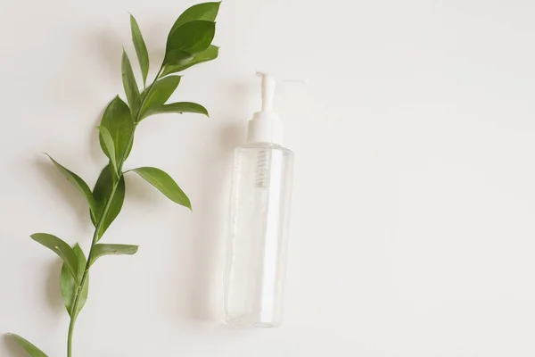 Une bouteille d'eau micellaire sur fond blanc avec une branche de feuilles vertes fraîches. Le concept de nettoyage de la peau, hydratant. Cosmétiques naturels d'extrait de fleur, de beauté et de mode — Photo