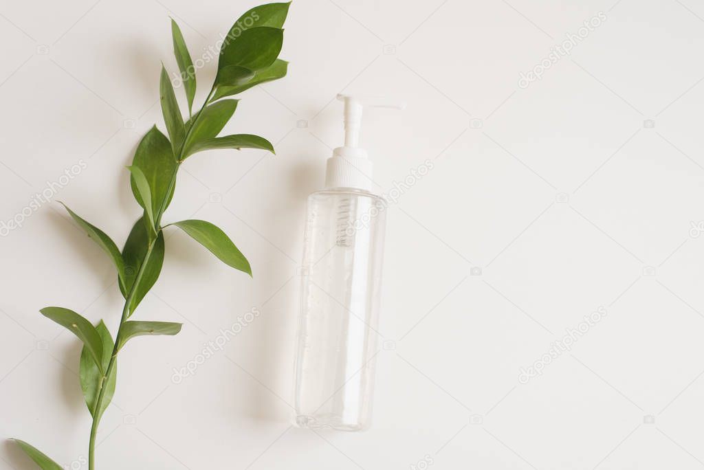 A bottle of micellar water on a white background with a branch of green fresh leaves. The concept of skin cleansing, moisturizing. Natural cosmetics from flower extract, beauty and fashion