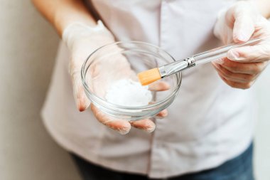 Kozmetoloji için reklam kampanyası. Beyaz elbiseli ve eldivenli kız maskeyi beyaz arka planda bir kasede karıştırıyor.