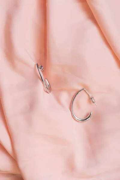 Pendientes de plata sobre un costoso fondo de seda rosa pálido. Hermosa joyería femenina. Pendientes anillos . — Foto de Stock
