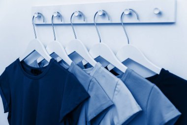 Klasik mavinin farklı tonlarında tişörtler bir mağazadaki askıda asılı duruyor. Bir alışveriş merkezinde kıyafet seçip satmak. Yıl Rengi 2020 konsepti.