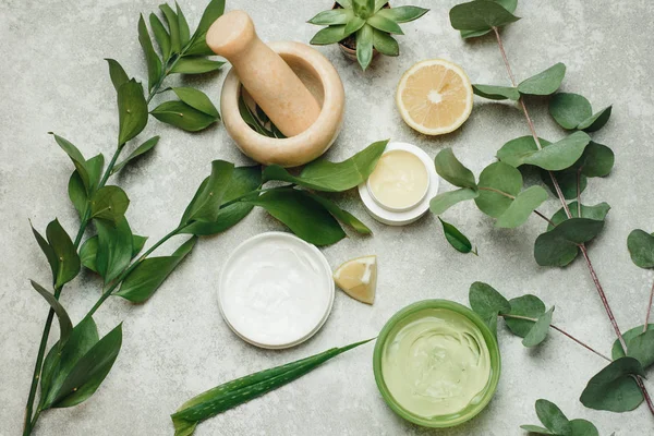 Flat lay composition with cosmetic products on grey background. Cans of natural cream and gel, mortar for mixing ingredients. Natural skin care beauty products