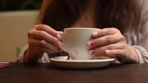Dívka pije kávu z bílého hrnku v kavárně. žena středního věku sedící v kavárně s šálkem čaje nebo kávy a polykající. Detailní záběr rukou s pohárem — Stock video
