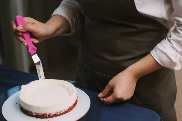 O confeiteiro nivela o creme no bolo. O cozinheiro cria um bolo, recolhe-o e cobre-o com creme e depois nivela-o com uma espátula e um raspador. — Fotografia de Stock