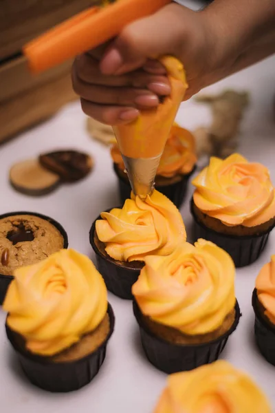 El confitero aprieta la crema de naranja sobre los cupcakes. Cocinar decorar cupcakes con crema — Foto de Stock