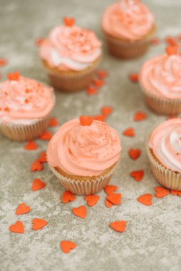 Pink cupcakes on a gray background for Valentine's day. Gift sweets with cream and sprinkle with hearts