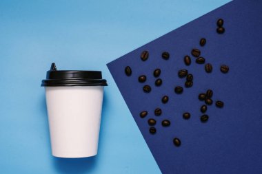 Kahveli kahve çekirdekli mavi ve cyan arka planda plastik kapaklı beyaz mukavva cam. Bir bardak hazır kahveyle birlikte. Moda rengi klasik mavi. Kopyalama alanı, düz uzanma