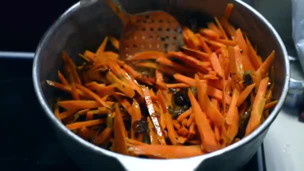 The cook mixes the meat with carrots in the broth. Cooking in a cast-iron cauldron close-up. The cook adds chopped carrots to the pan with hot oil and mixes with a metal spoon. Traditional oriental — 비디오