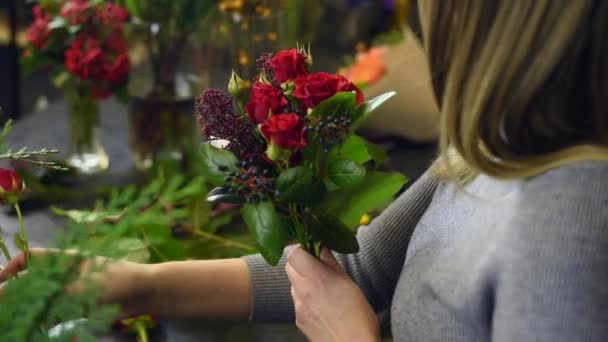 Krásná dívka sbírá ve svém ateliéru tmavou kytici rudých růží. Muž květinářství vytváří krásné kytice v květinářství. Doručování květin, vytváření pořádku, Malé podniky — Stock video