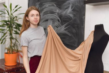 Terzi dikiş atölyesinde siyah bir manken üzerinde kumaş deniyor. Tasarımcı bej kumaştan bir elbise tasarlıyor ve elbise yapıyor. Kadın terzi kumaşı iğneli mankene takıyor. Öldür