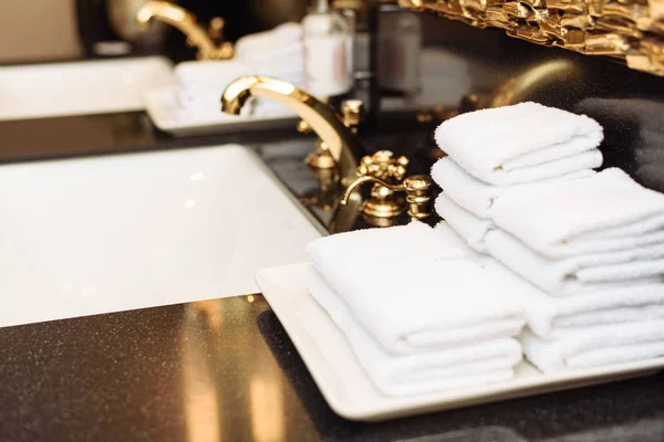 A stack of fresh white towels in the hotel 's luxurious bathroom. Золотой кран, зеркало и мраморная раковина в общественном туалете дорогого здания — стоковое фото