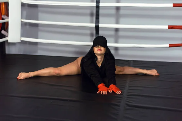 A girl sits on a split in a boxing ring. Sexy girl in a swimsuit bodysuit is stretched in the gym — Stock Photo, Image