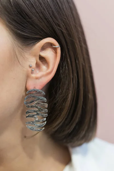 Trendy stylish silver earrings on the girl's ear with bob haircut. Pastel pink background — Stockfoto
