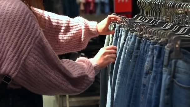 Piękna młoda dziewczyna wybiera dżinsy w sklepie. Kobieta zakupy dla dżinsów w sklepie odzieżowym — Wideo stockowe