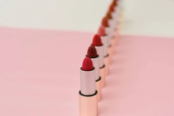 Una gran cantidad de diferentes lápices labiales de pie sobre un fondo beige y rosa. Patrón y concepto de belleza, cosméticos, accesorios para mujer. Tonos de tubos de lápiz labial — Foto de Stock