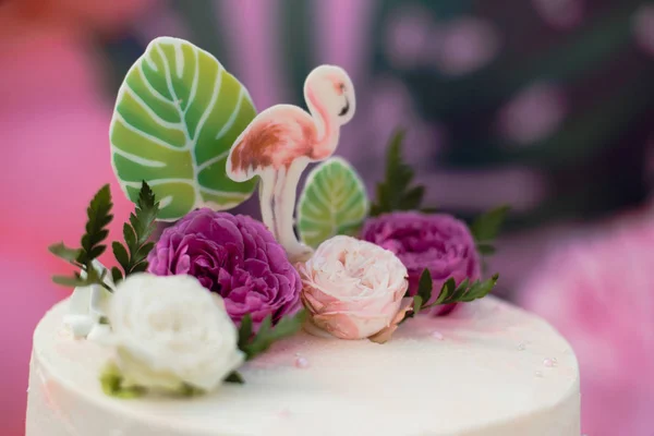 Pink cake with flamingos for the holiday. Cake with a variety of decorations, palm leaves and fresh flowers