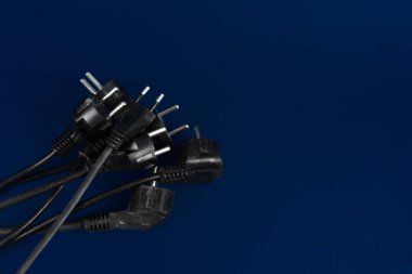 Old, used wires with plugs lie on a blue background. The concept of electricity, energy saving, the choice of electrical appliances and safety