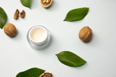 Yellow cream made from natural ingredients on a blue pastel background with green leaves and walnuts. The concept of creating essences from natural ingredients