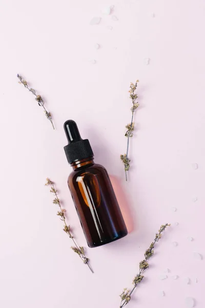 Suero hidratante para la cara en vidrio marrón oscuro sobre un fondo rosado junto a flores secas y sal marina. El concepto de crear cosméticos naturales y esencias a partir de ingredientes naturales —  Fotos de Stock