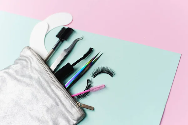 Bolsa cosmética de plata con un conjunto para la extensión de pestañas y teñido. Pinzas de extensión de pestañas, pestañas postizas, parches para los ojos y cepillo de cejas sobre un fondo pastel de moda — Foto de Stock