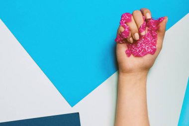 Çıplak manikürlü bir kızın eli, mavi pastel arka planda pembe bir yalama tutar. Günlük şablonu, manikür konsepti