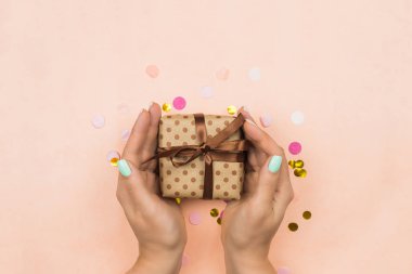 Kadının elleri pembe arka planda bir hediye verir. Blog ya da reklam şablonu. Pembe pastel arka planda çok renkli konfetiyle bayram hediyesi