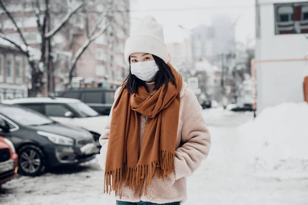 Passerby menina asiática em uma máscara médica protetora ao ar livre. Uma mulher na rua no inverno protege o trato respiratório da epidemia de coronavírus — Fotografia de Stock