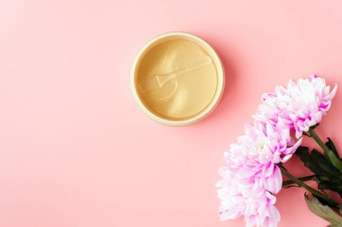 Pembe pastel arka planda, taze kasımpatı çiçeklerinin yanında altın lekeler. Doğal çiçek özütü kozmetik, güzellik ve moda. Bir kavanozda nemlendirmek için yamalar, düz uzanma, üst görünüm.