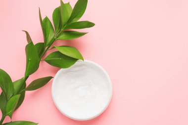 Cilt bakımı, gençleştirme ve yüzün sulanması anlamına geliyor. Patel pembe arka planda yeşil dallı nemlendirici krem..