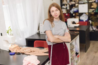 Dikiş atölyesinde kameraya bakan mutlu bir terzi. Elinde mezura taşıyan ve tekstil fabrikasında çalışan güzel bir terzinin portresi..