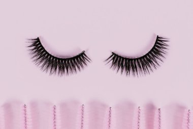 Pembe renkli pastel arka planda uzatılmış kirpikleri taramak için siyah sahte kirpik ve fırçalar. Sahte kirpikler, aplikatör ve fırçalar. Güzellik salonu. Makyaj malzemeleri. Üst manzara, düz uzanma.