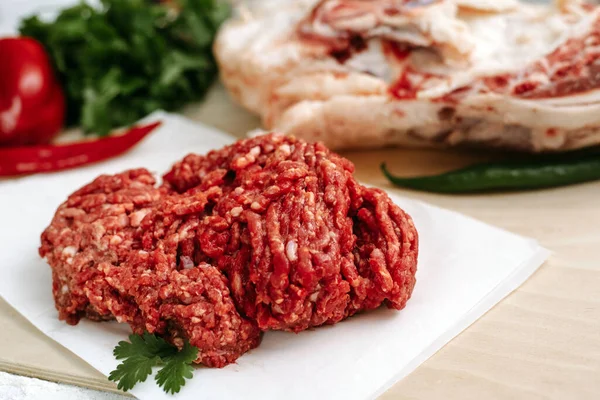 Red fresh minced meat on the background of lamb legs, red pepper and greens. Ground beef on the background of fresh meat in the kitchen of a housewife.