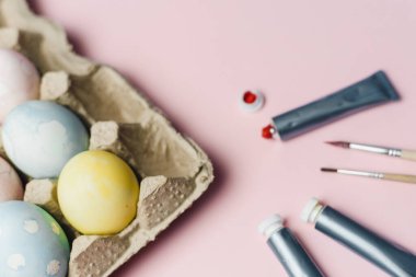 Paskalya yumurtalarını pastel suluboya renklerle boyama kavramı. Pembe arka planda Paskalya için yumurta boyamak için boya ve fırçalar.