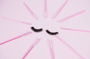 Pembe renkli pastel arka planda uzatılmış kirpikleri taramak için siyah sahte kirpik ve fırçalar. Sahte kirpikler, aplikatör ve fırçalar. Üst manzara, düz uzanma.