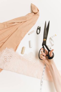 Masadaki makas ve kumaşın arka planındaki terzi kadın eli. Makas, kumaş, dikiş makinesi, beyaz arka planda santimetre ve iplik. Düz yatış, üst görünüm.